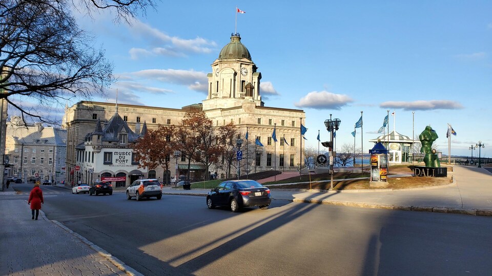 L'ancien bureau de poste de Québec en arrière-plan, près de la terrasse Dufferin. Une dame marche dans la rue, quelques voitures circulent.