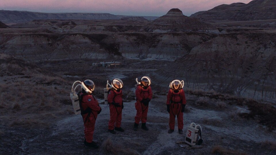 Quatre astronautes son assemblés en demi-cercle dans une vallée sur la planète mars. 