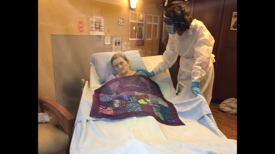 Ann Bérubé étendue dans son lit, une infirmière lui pose la main sur l'épaule. 