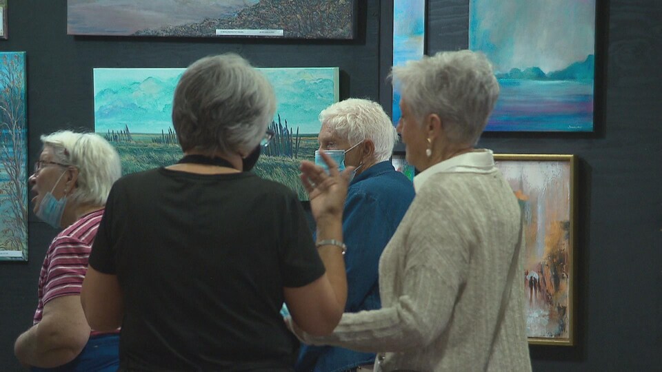 Des visiteurs masqués se pressent devant des peintures d'artistes.