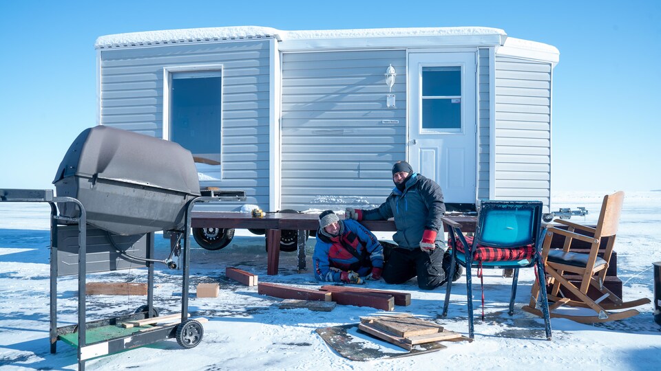 Deux personnes installent une cabane sur la glace.