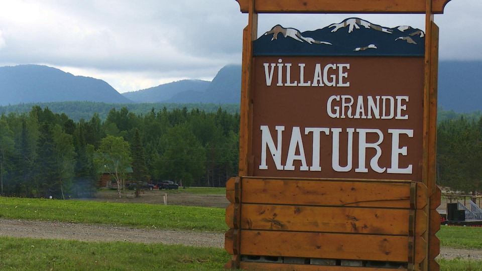 Un grand panneau de bois avec l'inscription Village grande nature devant un paysage de montagnes.