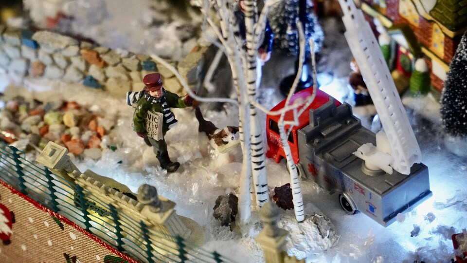 Un petit livreur de journaux avec son chien dans la neige dans un village miniature de Noël.                                
