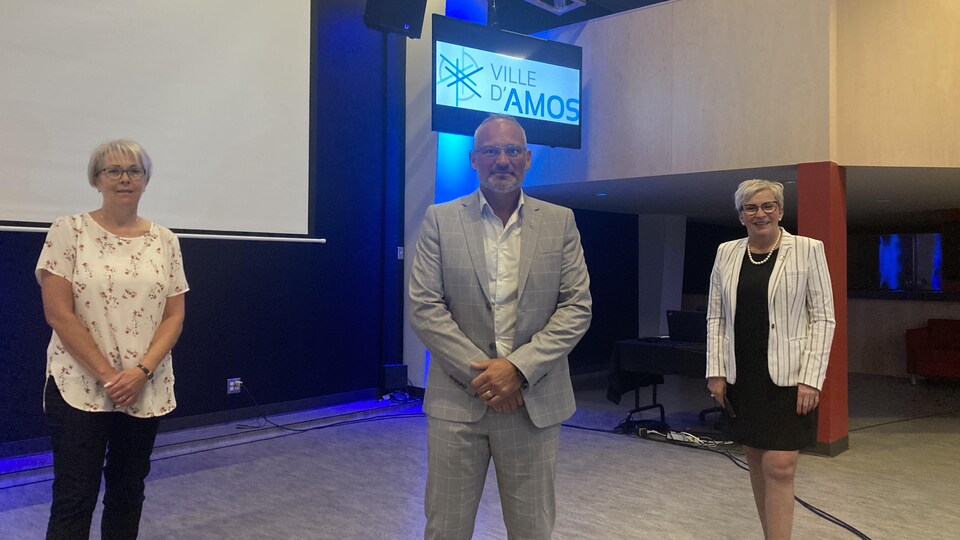 Les trois posent dans une salle avec un écran indiquant Ville d'Amos.