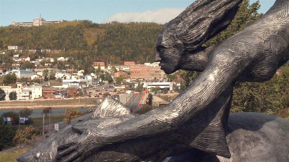 Un bronze d'une femme et d'un poisson en avant-plan de la ville de Gaspé.