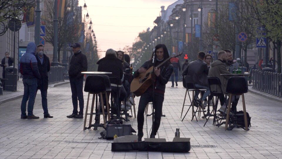 Un musicien s'exécute près de clients attablés en pleine rue.