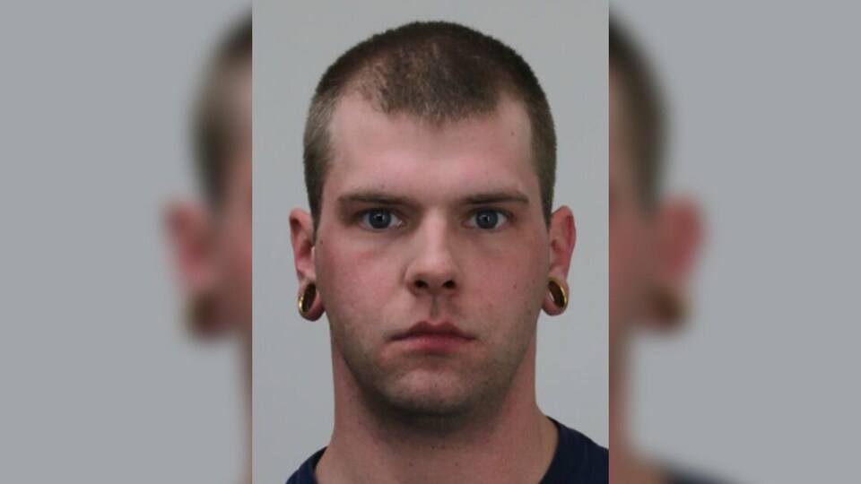 Un homme aux cheveux très courts avec deux grosses boucles d'oreilles de type « stretch ».