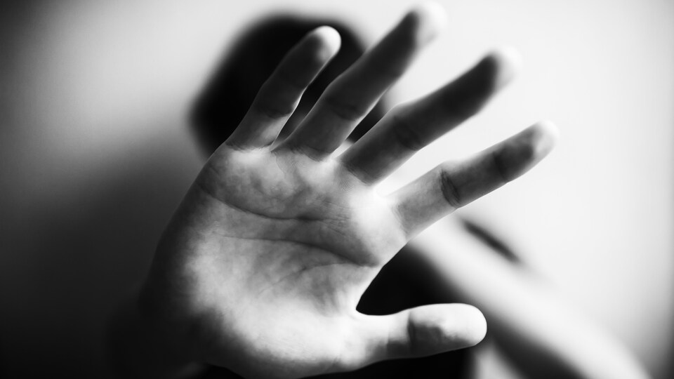 Une personne montre la paume de sa main pour se protéger.