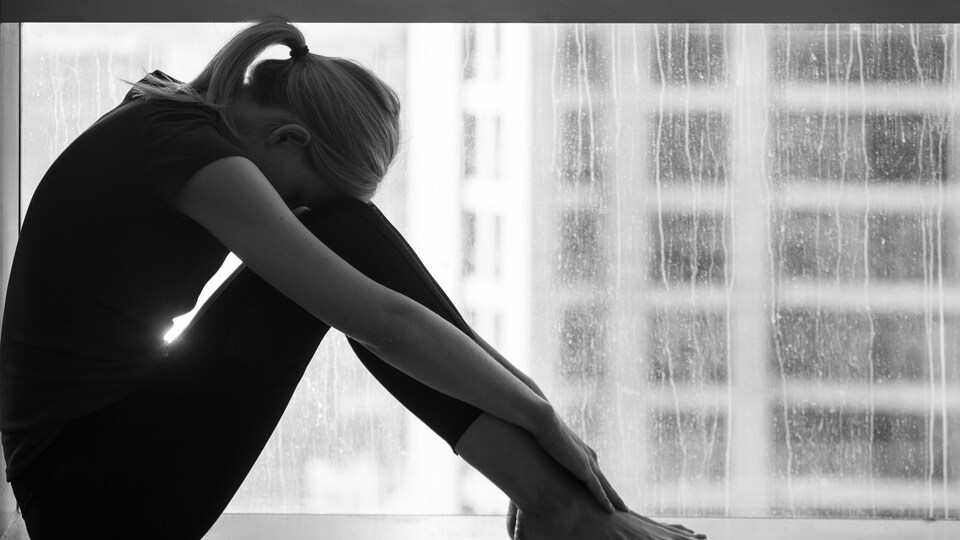 Une femme triste assise au bord d'une fenêtre.