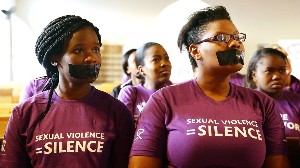 Elles ont la bouche couverte de ruban adhésif noir et portent un chandail sur lequel est écrit « Violence sexuelle = silence ».
