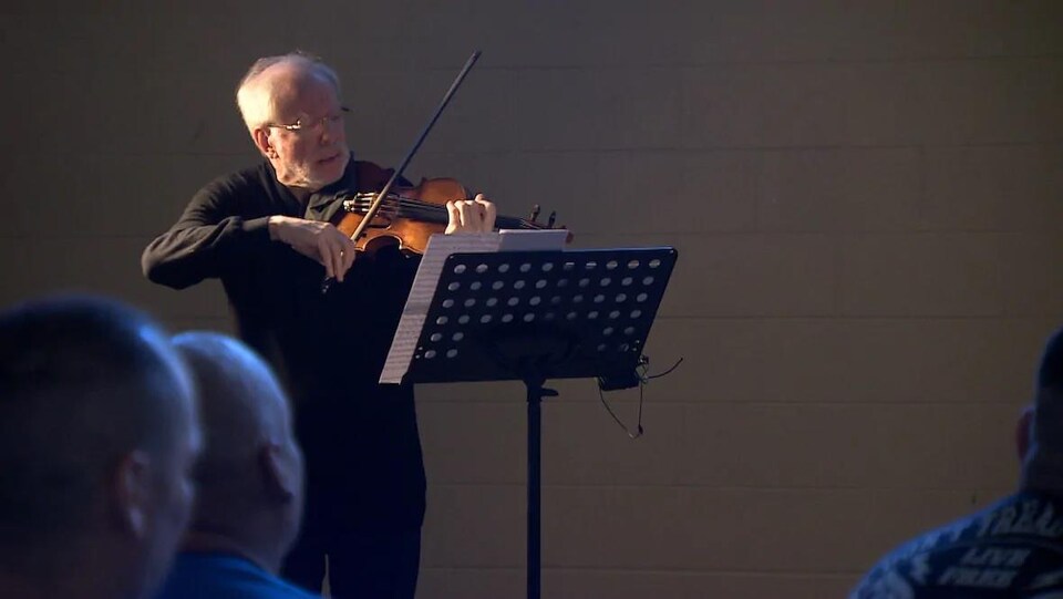 Le musicien Gidon Kremer joue du violon en regardant une partition sur un lutrin.