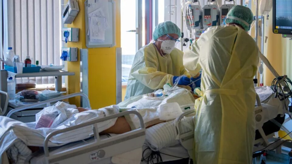 Un patient couché avec un soignant dont on voit le corps et les mains.
