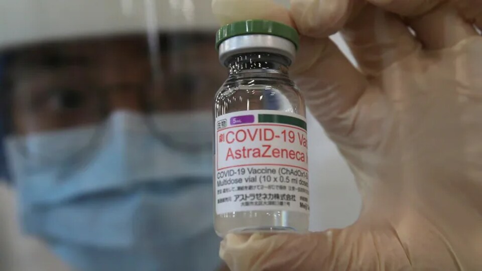Un travailleur de la santé masqué tient une bouteille de vaccin AstraZeneca.