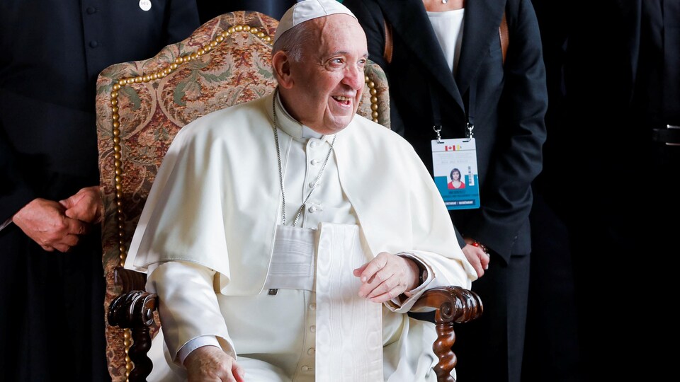 Le pape, assis, sourit.
