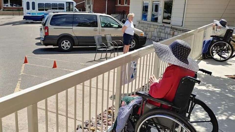 Deux personnes visitent, à l'extérieur, une résidente d'un centre de soins.