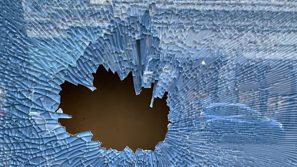 Une vitre cassée, dans laquelle on voit le reflet d'un bâtiment et une voiture, à Victoria, le vendredi 13 mai 2022.