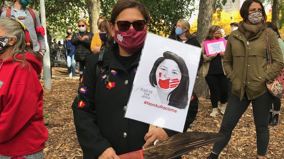 Une femme innue masquée porte une pancarte de Joyce Echaquan.