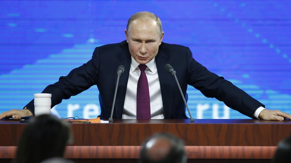 Le président russe, les mains posées sur une table, regarde devant lui en s'afdressant aux journalistes.