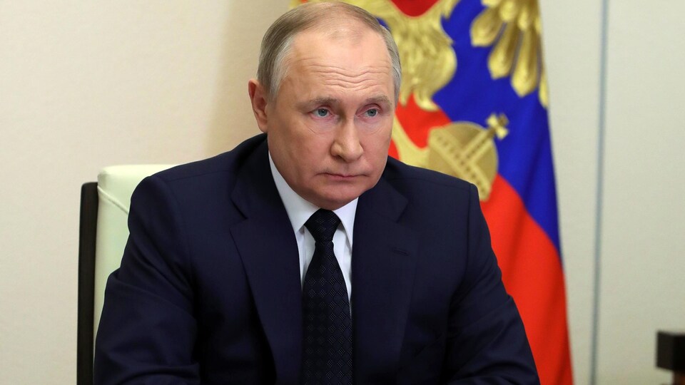 Vladimir Poutine est assis à une table devant un drapeau de la Russie.