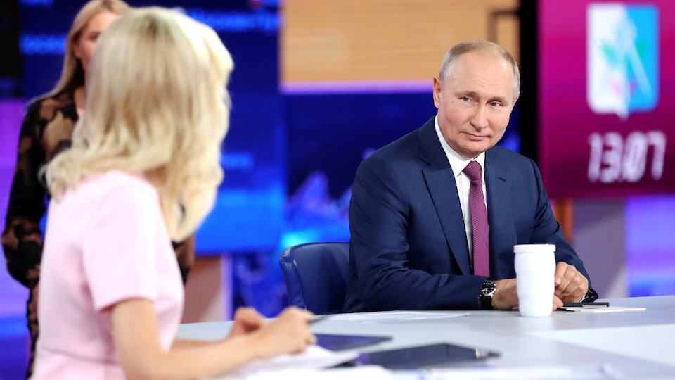 Vladimir Poutine regardant la présentatrice avec un petit sourire.