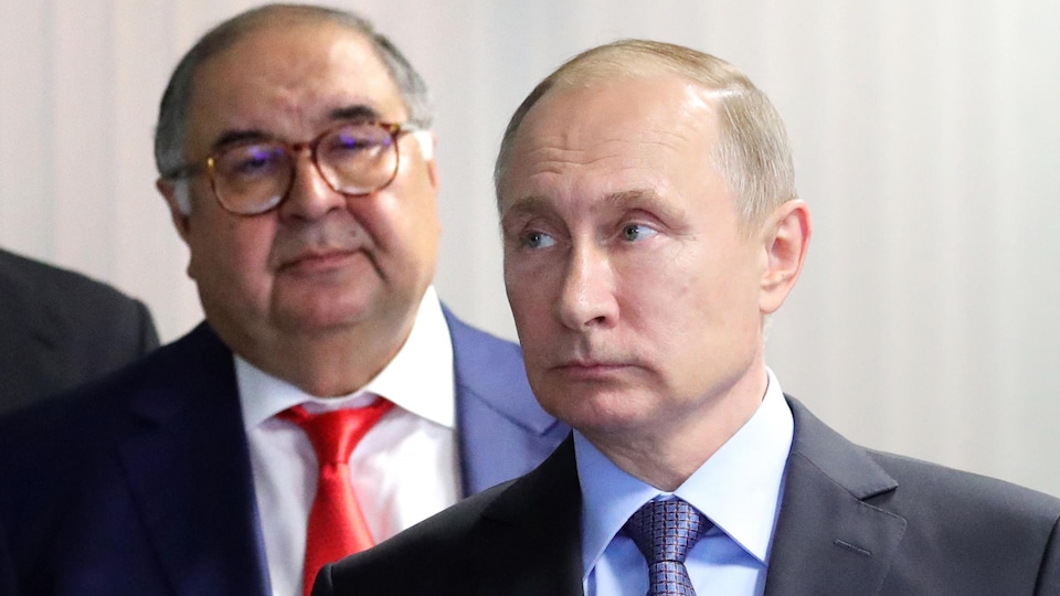 Vladimir Poutine regarde au loin. Derrière lui, Alisher Usmanov le regarde.