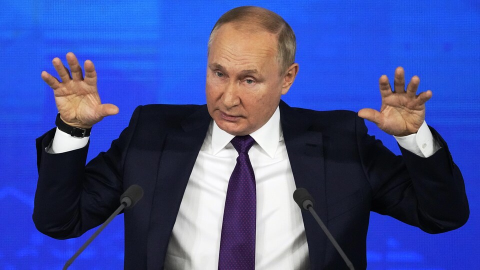 Vladimir Poutine, les mains en l'air, assis à une table, derrière des micros.