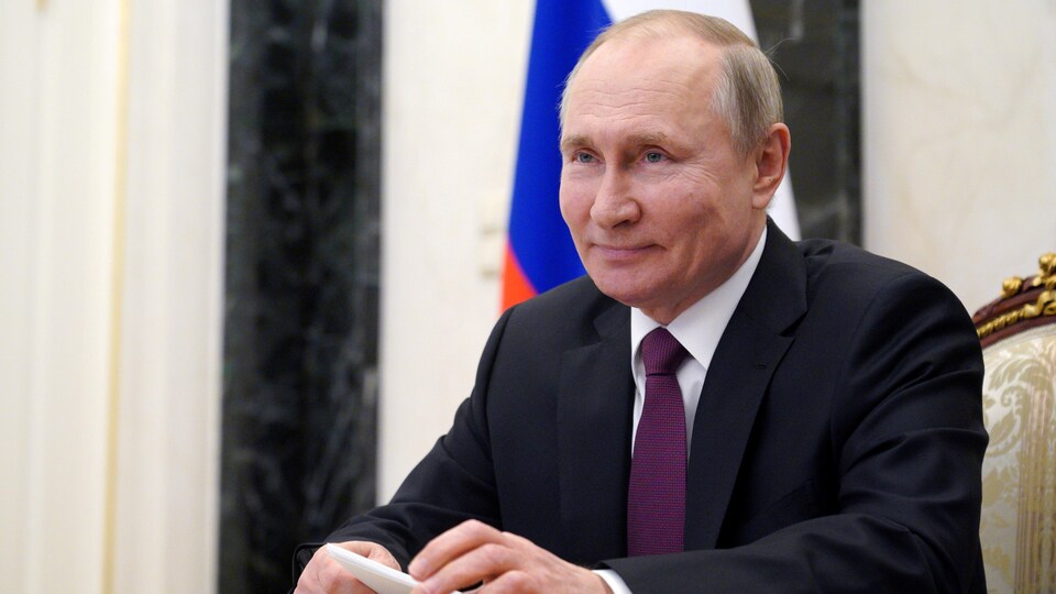 Vladimir Poutine est assis à un bureau et tient une liasse de papiers dans ses mains. 