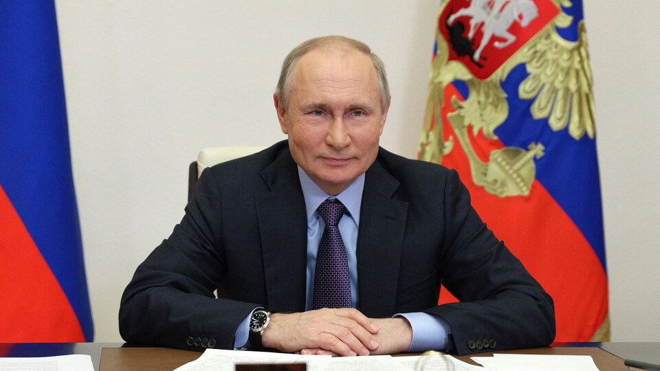 Vladimir Poutine, assis à un bureau avec des drapeaux russes derrière lui.
