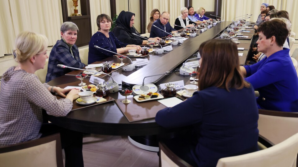 Le président Poutine est en compagnie d'une quinzaine de femmes assises à une table dotée de micros. 
