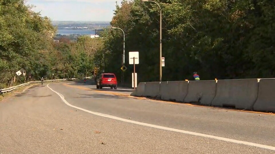 Un véhicule et des cyclistes circulent sur la voie Camillien-Houde, sur le mont Royal.