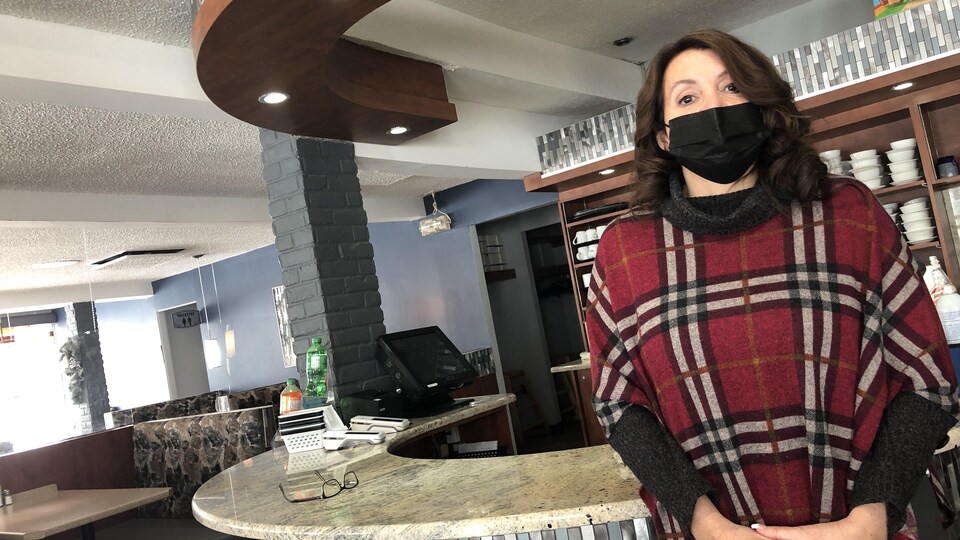 Une femme portant un masque parle dans son restaurant vide.