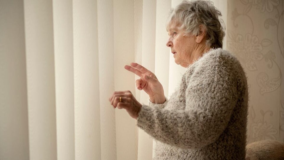 Une dame surveille ses voisins par la fenêtre.