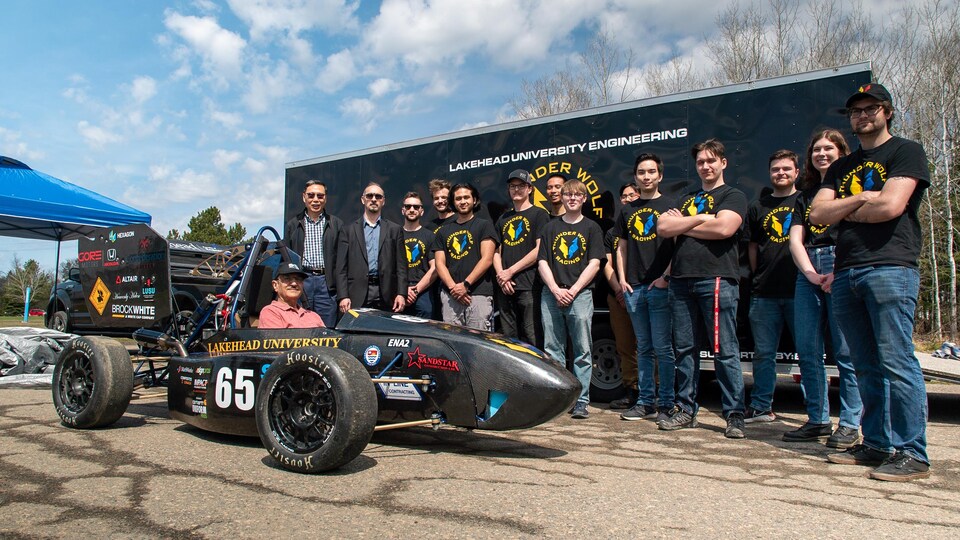 Des étudiants posent pour une photo près d'un voiture de course.