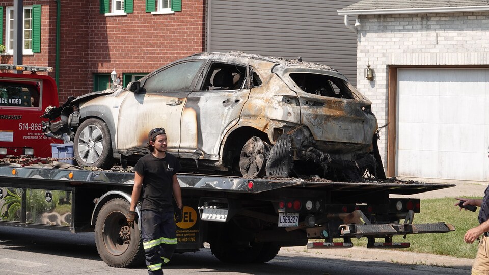 Un employé d'une entreprise de remorquage marche devant la carcasse calcinée d'une voiture.