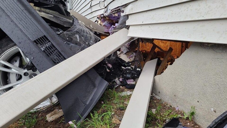 On voit la voiture accidentée et un trou dans la fondation de la maison, à travers duquel on peut voir le sous-sol de la demeure.