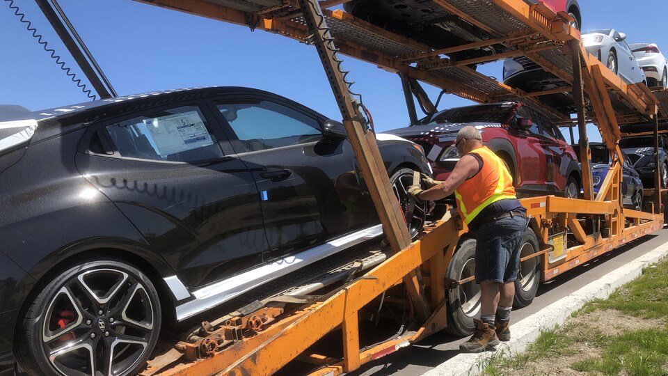 Un homme sort des voitures neuves qui sont installées sur une remorque. 