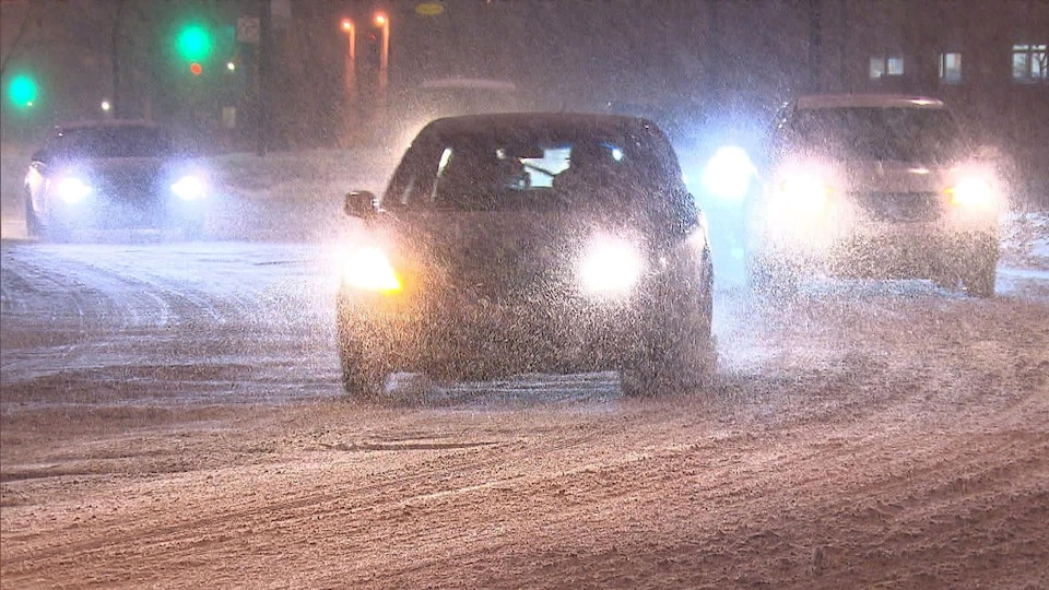 Des voitures circulent sur une route enneigée, en pleine tempête hivernale.