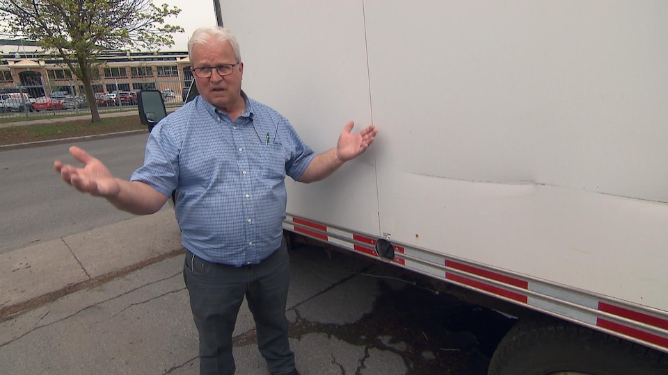 Bras en l’air, Pierre Gravel se tient debout à côté d’un camion.