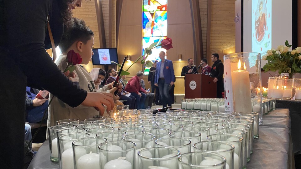 Une mère et son enfant tiennent chacun une rose rouge dans la chapelle de l'Université de la Saskatchewan. Ils se préparent à allumer une bougie. 