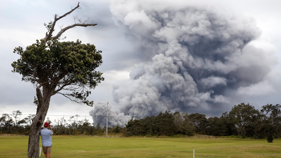 Un homme regarde au loin les éruptions du volcan Kilauea, qui assombrit le ciel de fumée.