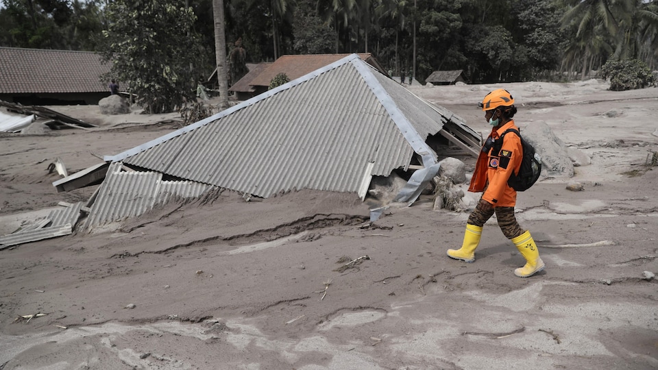 Un secouriste passe près d'une maison enterrée de boue grise jusqu'au toit.