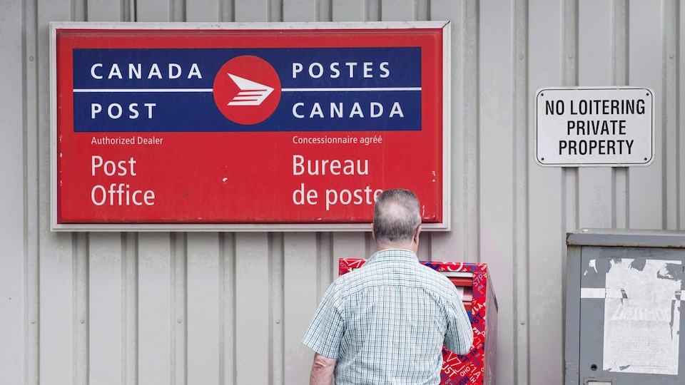Un homme dépose une enveloppe dans une boîte postale.