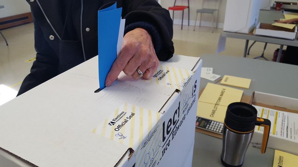 Un homme glisse un bulletin de vote dans la fente d'une boîte de scrutin.