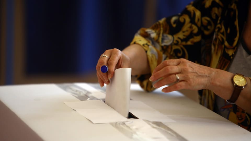 Les mains d'une personne qui met un bulletin de vote dans une urne.