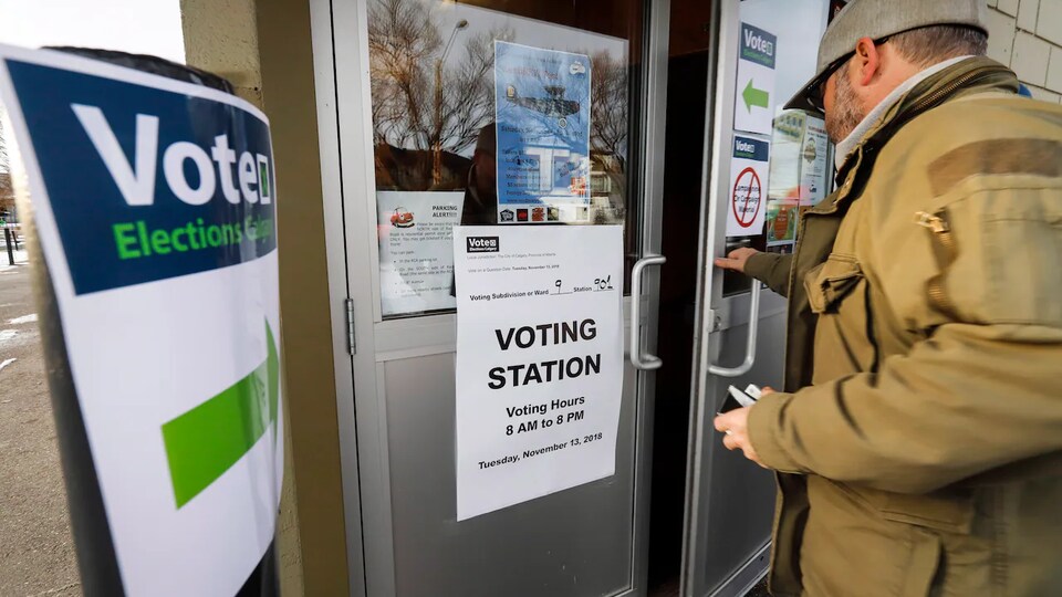 Un homme ouvre une porte où est posée une affiche indiquant qu'il s'agit d'un bureau de vote.