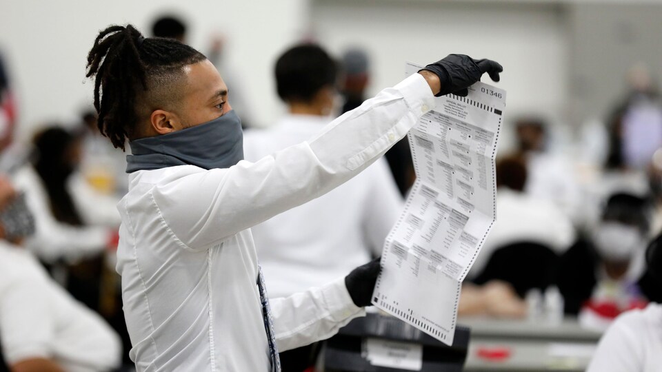 Un travailleur d'élection tient un bulletin de vote à la hauteur de ses yeux.