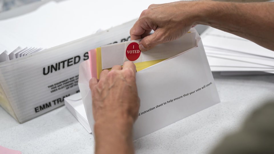 Quelqu'un insère des documents, dont un autocollant disant «J'ai voté», dans une enveloppe.  