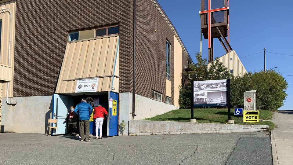 Un homme et une femme entrent dans un bureau de scrutin à Rouyn-Noranda. Une autre femme sort par une autre porte.