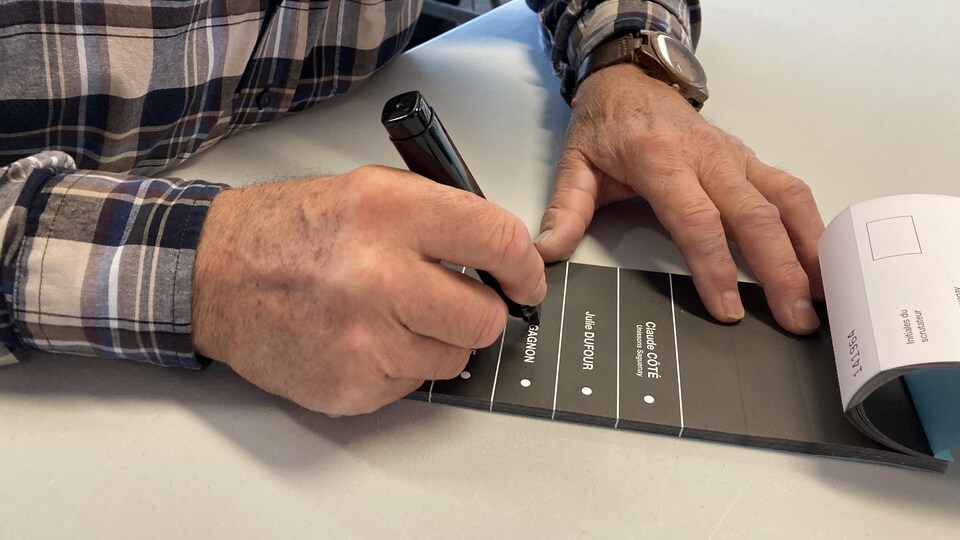 Des mains en gros plan barrent un nom au crayon feutre sur un bulletin de vote.