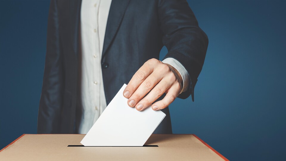 Un homme insère un papier, où il est inscrit son vote électoral, dans une boîte.